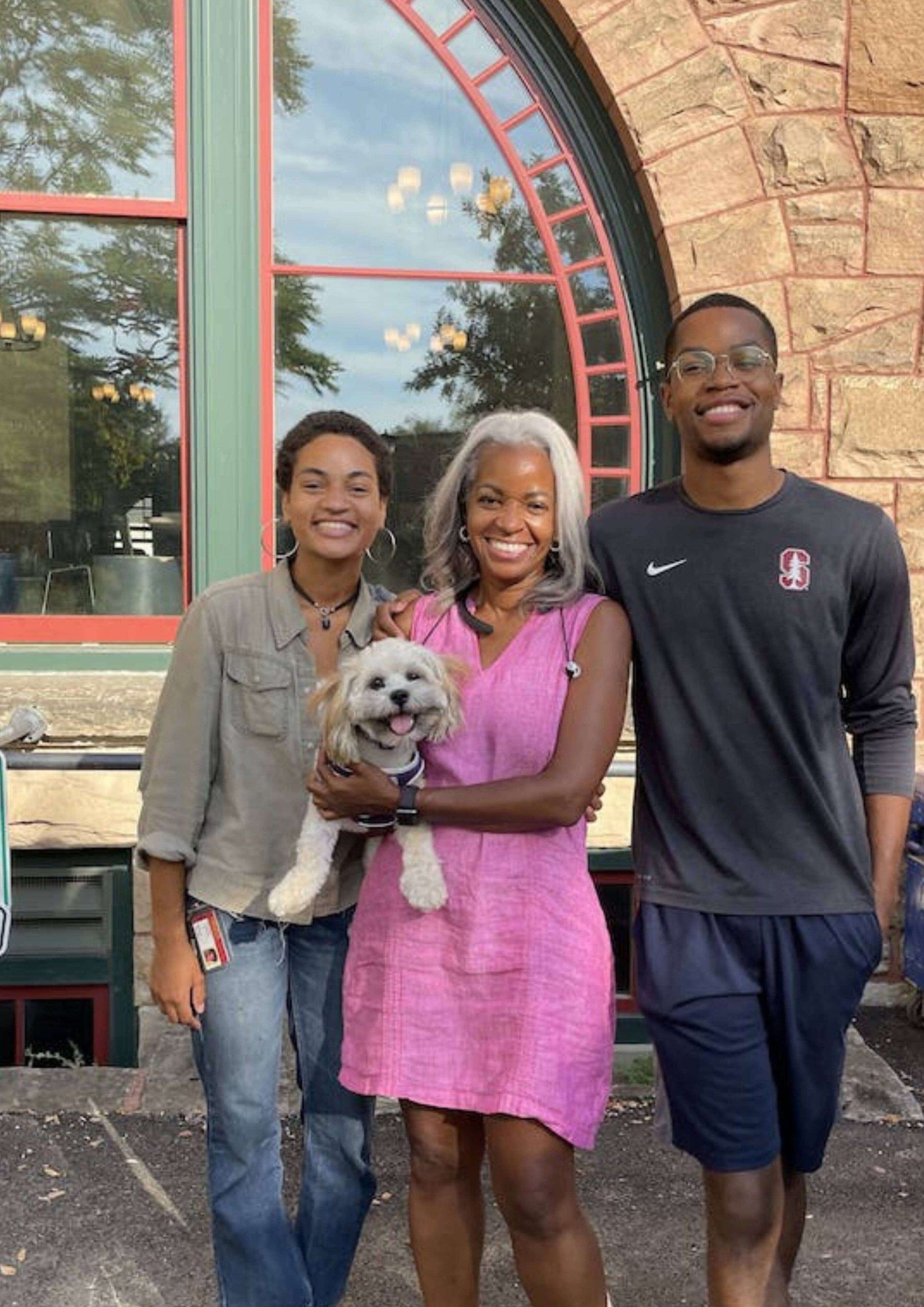 three smiling people one in middle holding a happy dog